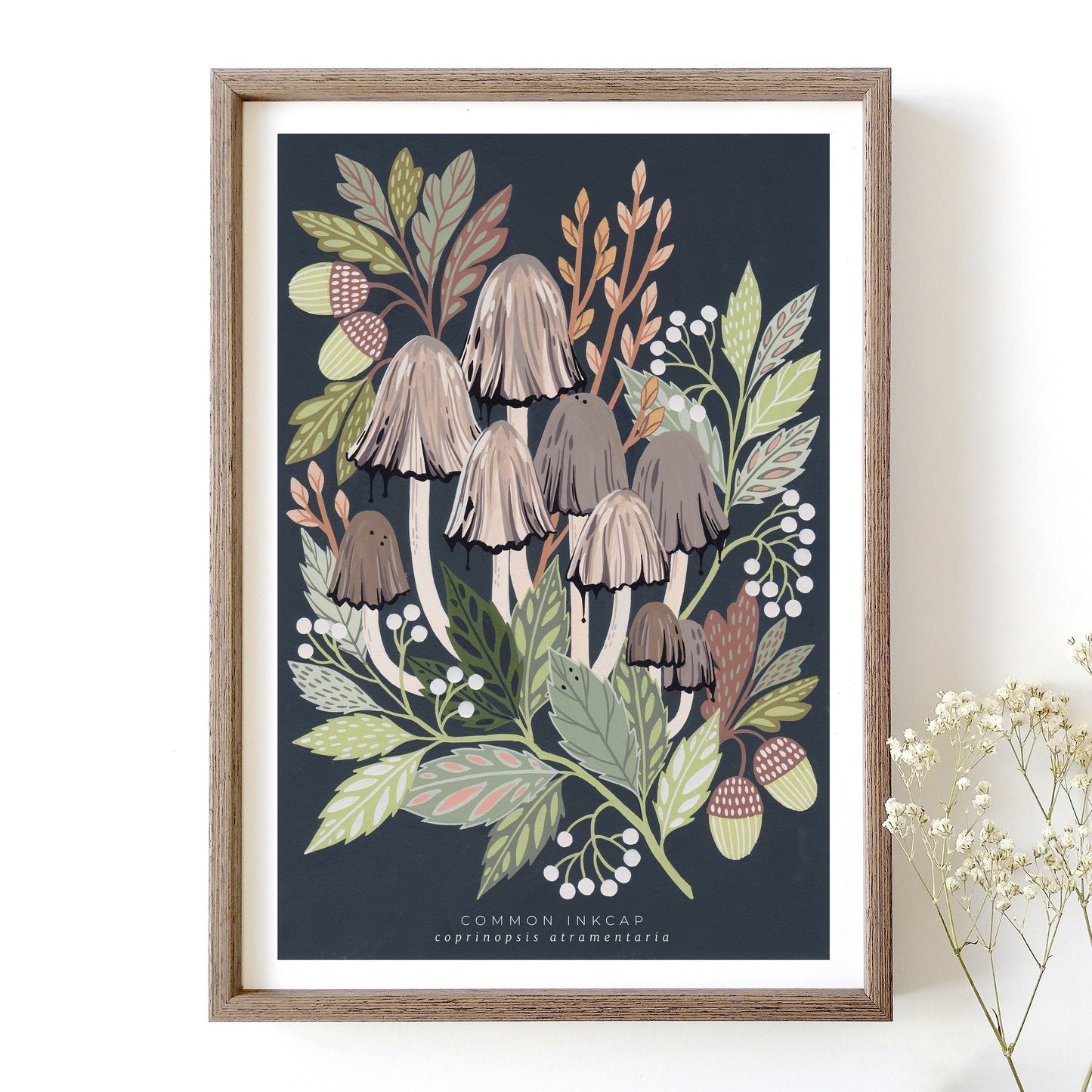 An art print featuring a cluster of common inkcap mushrooms with surrounding green leaves and dark background in a wooden frame.