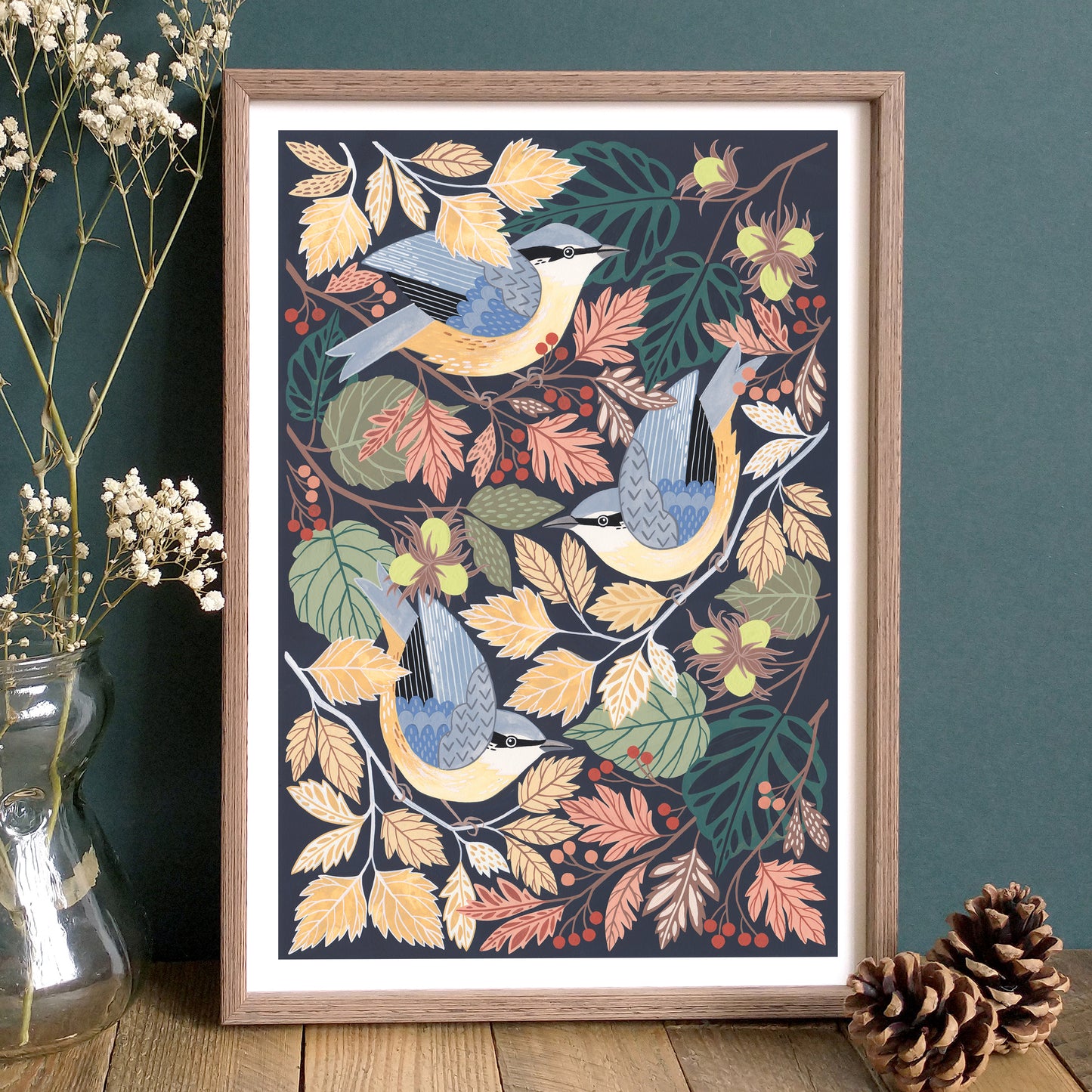 Framed artwork with nuthatches and autumn leaves on a dark background, displayed on a wooden surface.