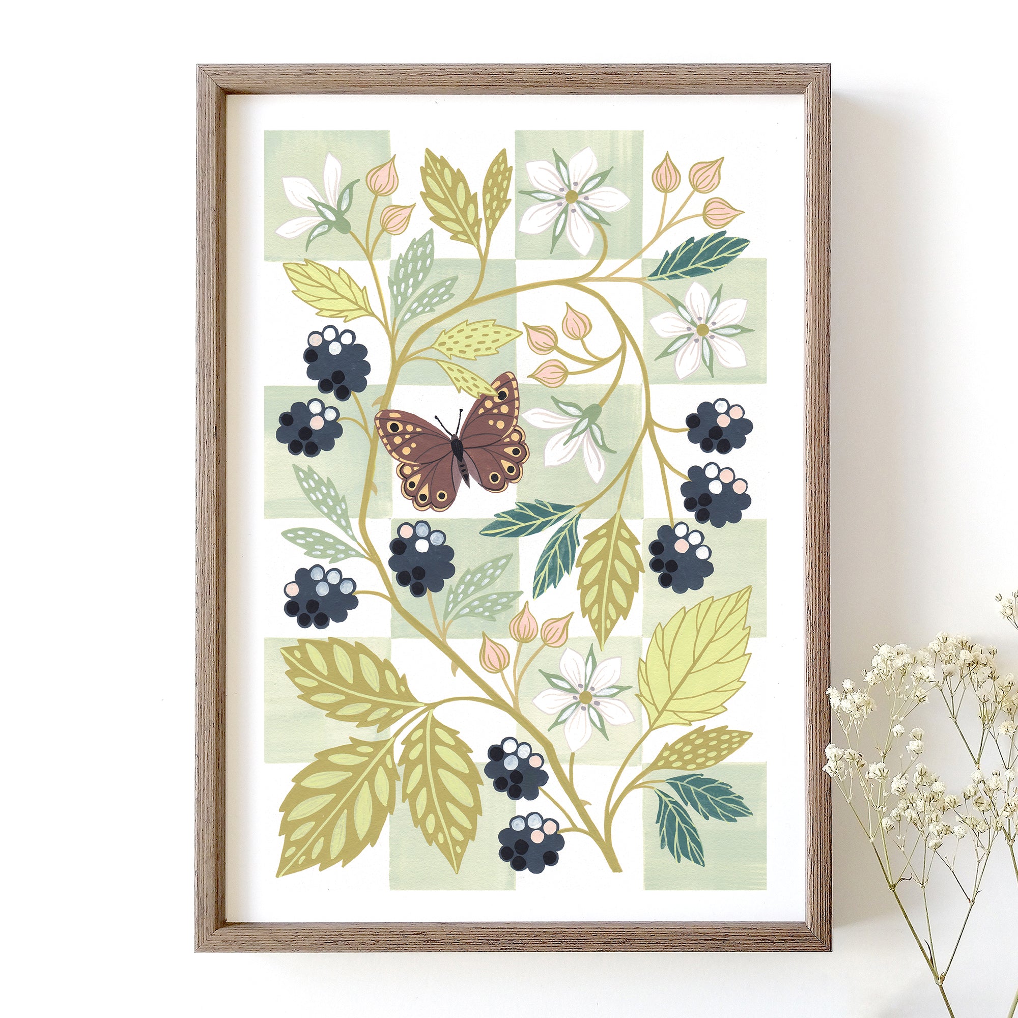 A framed botanical art print featuring a butterfly, blackberries, white flowers, and green leaves on a pale green chequered background.