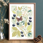A framed botanical art print featuring a butterfly, leaves, flowers, and blackberries.
