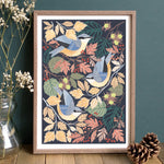 Framed artwork with nuthatches and autumn leaves on a dark background, displayed on a wooden surface.