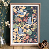 Framed artwork with nuthatches and autumn leaves on a dark background, displayed on a wooden surface.