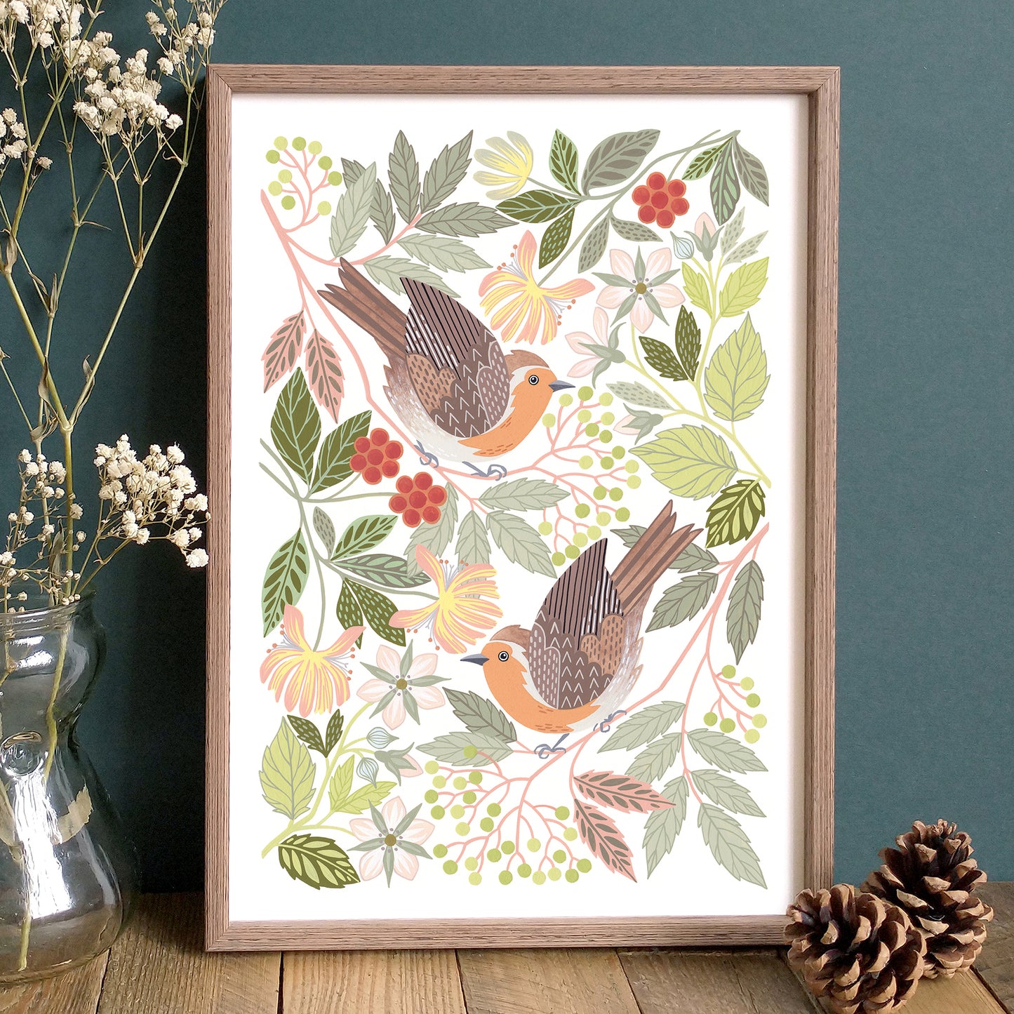 Framed artwork of robins and woodland foliage on a wooden surface with a dark blue wall background.