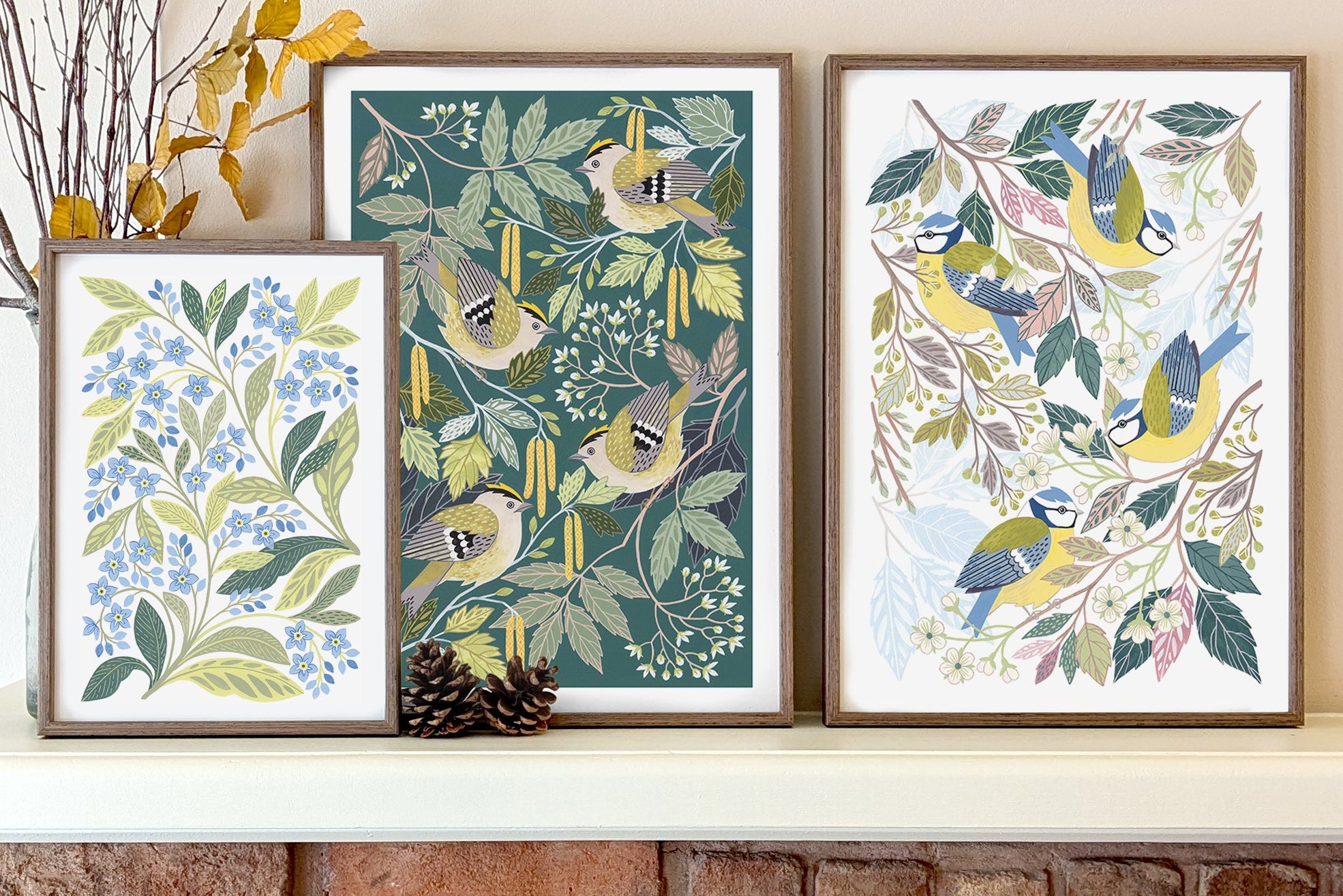 Three framed botanical and bird art prints displayed above a brick fireplace. 