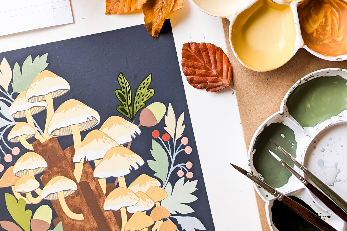 A flat-lay view of a painting in progress featuring mushrooms and autumn foliage, styled with paint palettes, brushes, and dried leaves on a white surface.