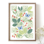 A framed botanical art print featuring illustrated green leaves, red strawberries, white flowers, and two blue butterflies.
