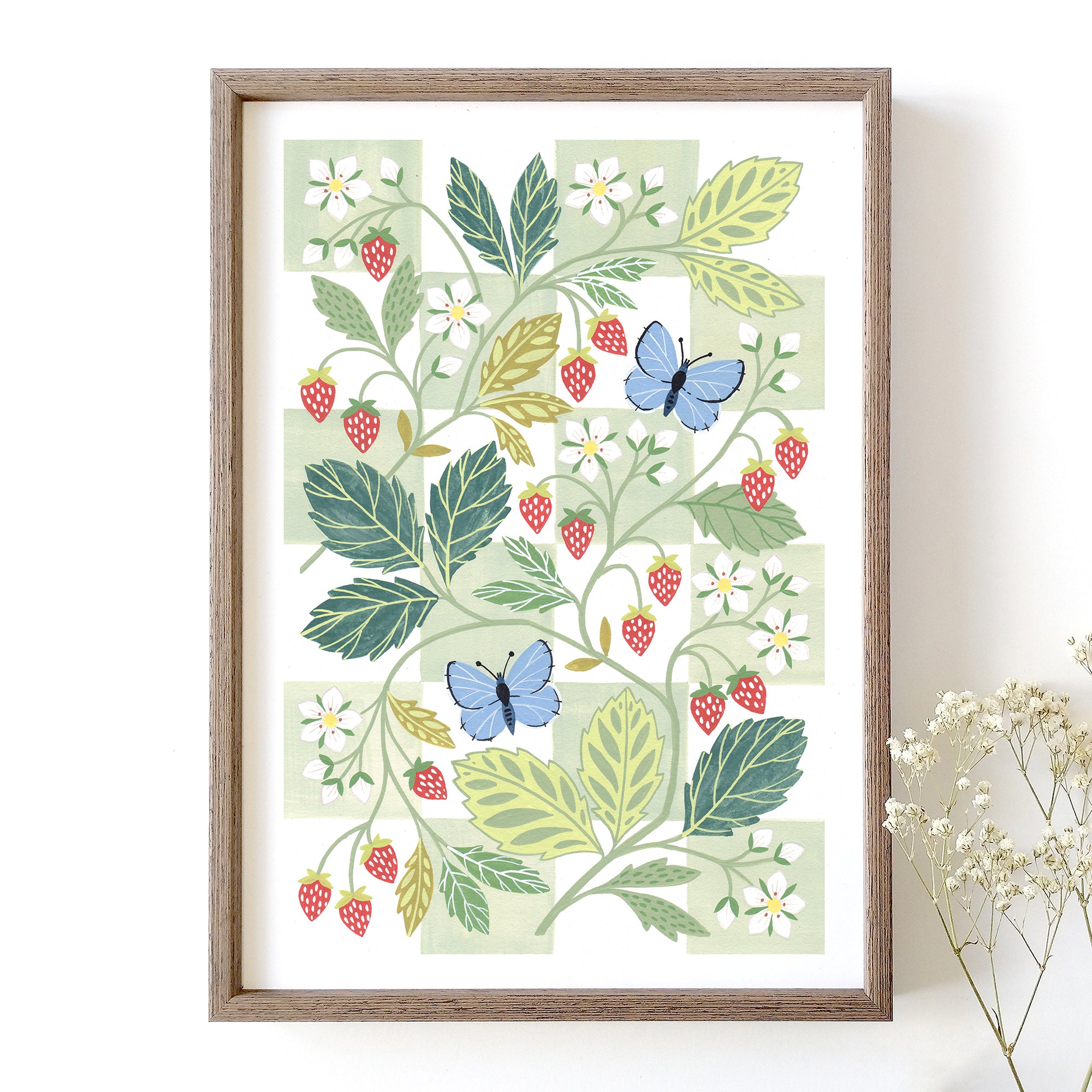 A framed botanical art print featuring illustrated green leaves, red strawberries, white flowers, and two blue butterflies.