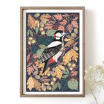 Framed artwork of a woodpecker among autumn leaves on a white wall.