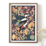 Framed artwork of a woodpecker among autumn leaves on a white wall.