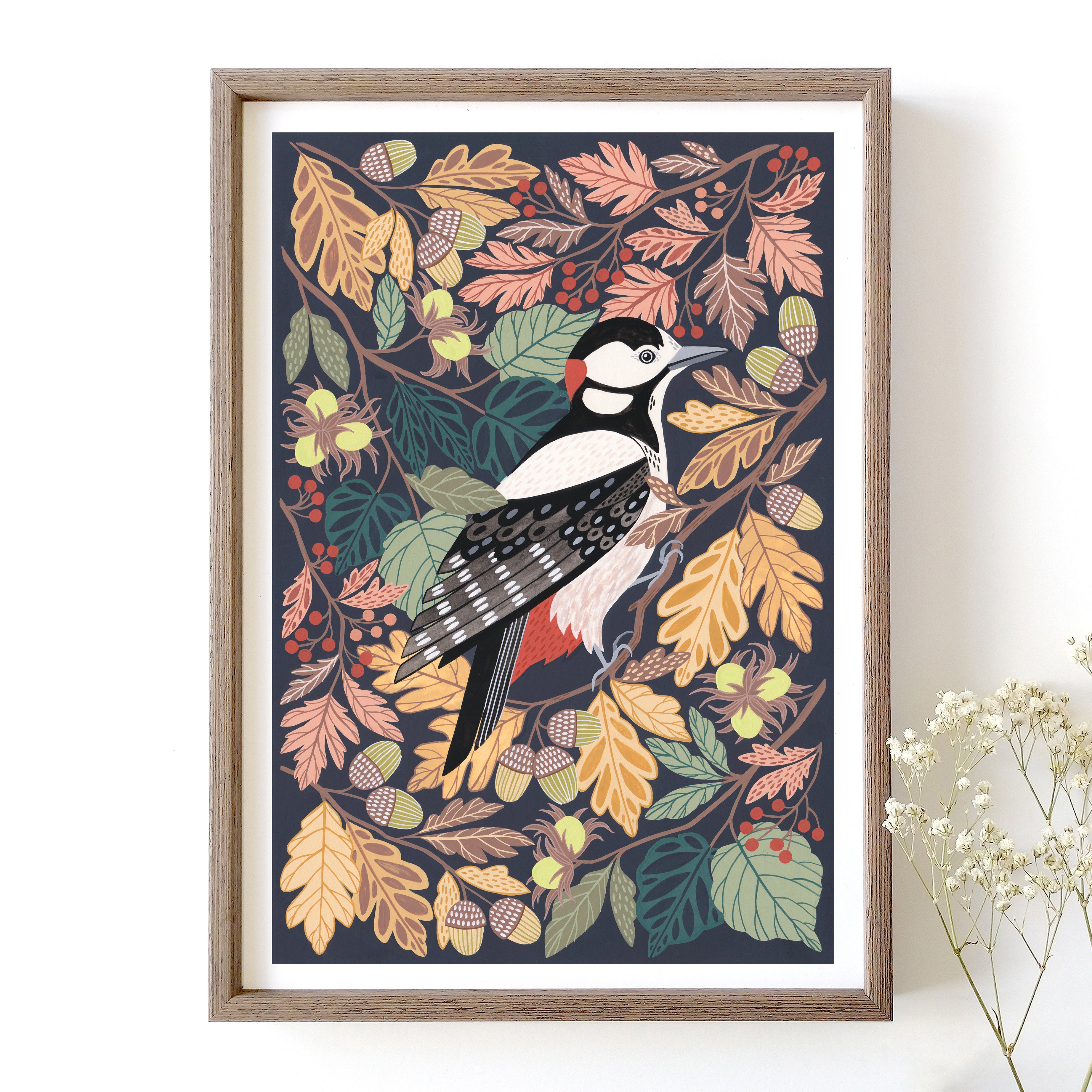 Framed artwork of a woodpecker among autumn leaves on a white wall.
